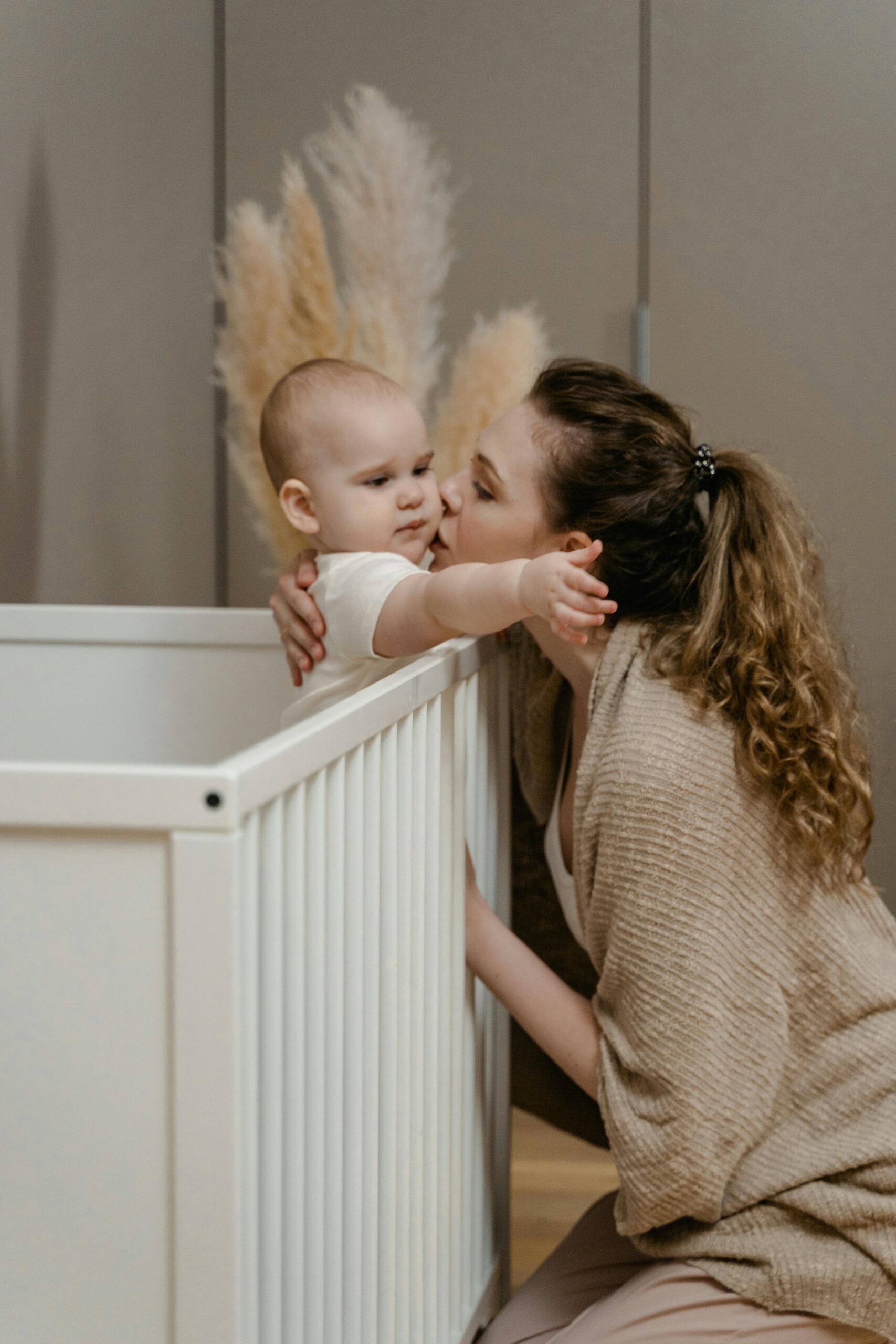 A tender moment of a mother kissing her baby as they laugh together in their cozy home.